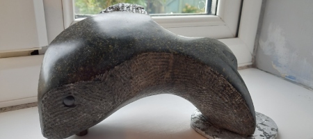 A table top sculpture of a leaping fish in shiny black polyphant stone with a silvered slate basebase